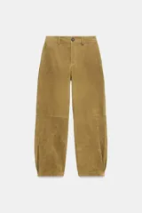 Pantalón de piel color tostado, tiro medio con cierre frontal de cremallera y botón, bolsillos delanteros y traseros, y bajo con acabado de pliegues.