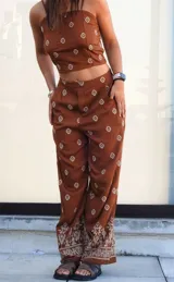 Conjunto de dos piezas compuesto por un top corto tipo strapless y un pantalón de corte holgado, ambos en color marrón con estampado geométrico étnico. El pantalón presenta un diseño de pierna ancha con detalle de guarda decorativa en el ruedo.