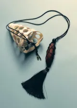 Collar largo ajustable con cordón negro, cuenta con un dije central de madera revestido en red negra y una borla colgante de flecos en la parte inferior.