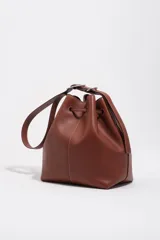 Bolso tipo saco de cuero marrón con cierre de cordón ajustable, asa larga regulable y logotipo de BIMBA Y LOLA impreso en el frente con letras blancas.