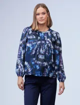 Blusa de gasa estampada con diseño circular en tonos azules, violetas y verde. Delantero plisado, puños elastizados, espalda con abertura ojal y botón.