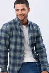 Camisa de viyela de manga larga con estampado de cuadros en tonos verdes y azul marino. Presenta cuello clásico con botones, cierre frontal abotonado y un bolsillo en el pecho.