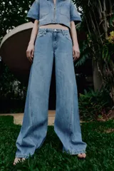 Jeans de tiro alto con pernera ancha y costuras marcadas en el frente. Presenta cintura elástica en la parte posterior, cierre frontal con cremallera y botón, bolsillos delanteros y bolsillos de plastrón en la parte trasera.