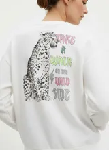 Buzo blanco de algodón y poliéster con cuello redondo y hombros caídos. Presenta un estampado grande en la espalda con un leopardo sentado y el texto "TAKE A WALK ON THE WILD SIDE" en tonos rosa, verde lima y plateado.