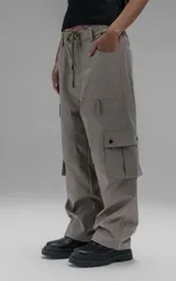 Pantalón cargo de corte oversize y silueta estructurada, confeccionado en microfibra pesada con leve elasticidad. Presenta cintura elástica con cordón de ajuste externo, cierre frontal con botón metálico, bolsillos laterales y bolsillos cargo de gran tamaño con tapa y broches a presión.