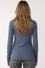 Remera blanca de manga larga, entallada, con cuello redondo y una hilera de botones en el frente. Incluye un pequeño bolsillo decorativo en el pecho.