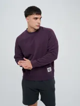 Buzo de felpa bordó, estilo relaxed, con cuello redondo y mangas raglán. Presenta puños y dobladillo acanalados, y una pequeña etiqueta con el logo de Umbro en el lateral inferior.