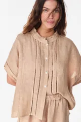 Camisa de lino marrón con mangas cortas, cuello mao con volados, cierre frontal con botones blancos y detalles de calados verticales en el frente.