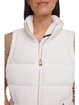 Chaleco blanco acolchado con cuello alto y cierre frontal con cremallera dorada. Tiene bolsillos laterales con cremallera y logo de la marca en el tirador.