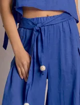 Pantalón palazzo de lino color azul, de tiro alto con cintura elastizada y cinto lazo incorporado con cuentas decorativas en las puntas. Presenta aberturas laterales pronunciadas en las piernas y corte amplio.