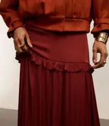 Falda midi evasé color borgoña de poliéster satinado, con cierre trasero invisible, volado en la cadera y ruedo fruncido.