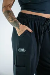 Pantalón de corte holgado y estilo urbano, color negro, con cintura elástica ajustable mediante cordón y bolsillos laterales. Presenta un pequeño estampado en la pierna derecha.