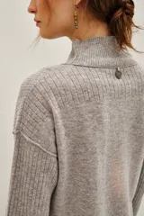 Polera de lana y cachemira color gris, con cuello alto y mangas largas con textura acanalada. Presenta un diseño holgado con aberturas laterales en el ruedo.
