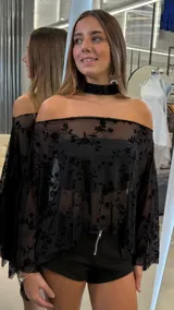 Top capa negro de tejido transparente con diseño flocado de flores, escote off-shoulder y mangas amplias. Incluye lazuelo para el cuello.