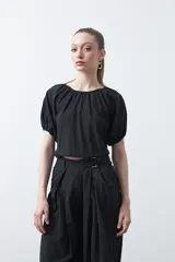 Top negro de manga corta con escote redondo y frunces en la costura de la sisa, creando un efecto de manga abullonada. El tejido parece ligero y con textura.