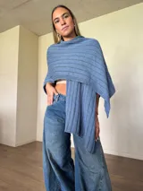 Ruana tejida de algodón con hilo lurex en punto jersey, color azul, con diseño amplio y detalle de etiqueta de cuerina en la parte posterior.