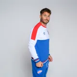 Buzo de cuello redondo Umbro del Club Nacional de Football. Diseño tricolor con cuerpo superior blanco, franja central azul y detalles en rojo en hombros y puños. Incluye logo de Umbro y escudo del club en el pecho.