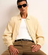 Campera color beige claro de algodón con textura arrugada, cuello inglés, cierre con cremallera, bolsillos laterales, elástico en la cintura y puños.