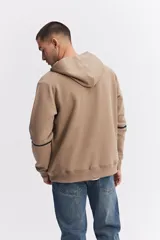 Campera con capucha y cierre frontal, color beige, con detalles de costuras y cierres en negro. Presenta mangas largas con puños acanalados y logo pequeño en el pecho.