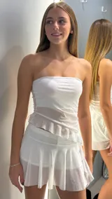 Short pollera de tiro bajo en color blanco, confeccionado en tela con acabado brillante y detalle de volado asimétrico en la cintura. El diseño combina la comodidad de un short con la estética de una minifalda.