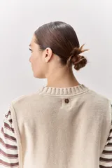 Chaleco tejido de punto color beige, con cuello redondo, terminaciones en rib y lazos laterales regulables que permiten ajustar la prenda.
