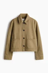 Campera camisera corta de sarga de algodón color verde militar, con cuello camisero, cierre frontal de botones oscuros y dos amplios bolsillos delanteros de parche.
