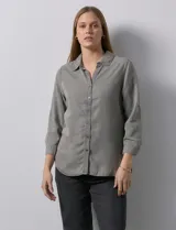 Camisa gris de tencel con cuello con solapa, escote en V y abertura central con botones. Largo de manga regulable con presilla y botón. Ruedo en espalda con tajo.