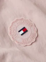 Rompevientos corto Tommy Hilfiger color rosa pálido, con cuello alto, cierre de cremallera, dos bolsillos laterales, detalles distintivos de la marca y logo engomado bordado en la manga.