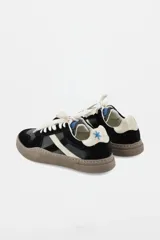 Zapatillas urbanas de cuero con paneles en gamuza negra y detalles en cuero color crema. Presentan suela de goma texturizada en tono marrón y cordones bicolores.