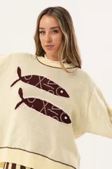 Sweater color manteca de tejido de punto con cuello redondo y ribete marrón. Presenta dos peces marrones tejidos en el frente con detalles bordados a mano.