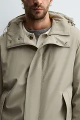 Parka de tejido técnico con acabado engomado, cuello subido y capucha ajustable. Presenta cierre frontal con cremallera oculta bajo solapa con botones a presión, bolsillos laterales de vivo y mangas largas con puños ajustables.