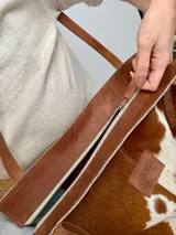 Bolso tipo tote Chabas modelo Molly, confeccionado en cuero con pelo natural en tonos marrón y blanco. Posee asas largas de cuero marrón, parche frontal con la marca grabada y un charm colgante decorativo en forma de estrella con detalle de pelo.