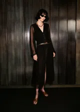 Vestido midi de gasa color negro, con cuello en pico, cierre frontal de botones y mangas largas abullonadas. Presenta un diseño recto con abertura frontal en el bajo y forro interior.