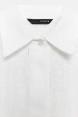 Camisa blanca de algodón con bordados florales, cuello solapa, manga corta, bolsillo de plastrón en el pecho y cierre frontal con botones ocultos.