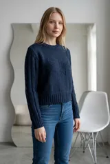 Sweater de punto color verde, con cuello redondo, diseño de trenzas en las mangas y detalle de relieve en el frente. Presenta un corte corto con puños y ruedo acanalados.