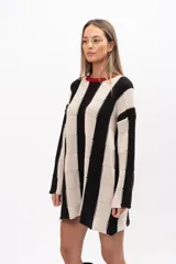 Buzo tipo poncho de corte oversize y holgado, con diseño de bloques verticales en colores blanco y negro. Presenta cuello redondo con detalle en color rojo, mangas largas y bolsillos laterales.