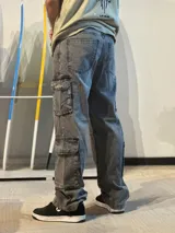 Jean baggy cargo color gris gastado, con tiro alto, piernas anchas y múltiples bolsillos laterales funcionales.