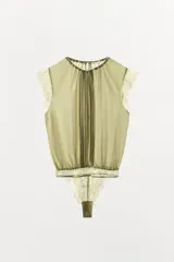 Body tipo blusa de georgette color verde oliva, con cuello redondo ajustable mediante lazada, mangas muy cortas con detalle de encaje y pliegues verticales en el delantero. Presenta una base de encaje en la parte inferior y cierre con botones a presión en el bajo.