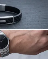 Pulsera masculina con banda de goma negra con textura de fibra de carbono y placa central de acero inoxidable.