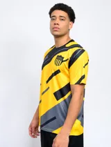 Remera de entrenamiento Fynar del Club Atlético Peñarol, color negro con estampado geométrico en amarillo y gris. Presenta cuello redondo, mangas cortas y el escudo del club en el pecho.
