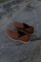 Zapatos tipo chelsea de cuero color marrón, con paneles elásticos laterales y suela plana de goma.