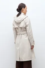Trench impermeable color beige de corte clásico, con cierre frontal de doble botonadura, solapas amplias y cinturón ajustable con hebilla. Incluye capucha desmontable y bolsillos laterales.