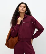 Campera deportiva de algodón color bordó, de cuello alto, con cierre frontal metálico y detalles de piping contrastante claro en el pecho y las mangas. Cuenta con bolsillos laterales y puños y dobladillo acanalados.