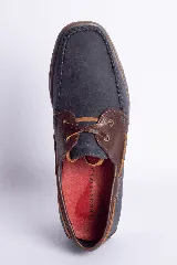 Zapato náutico de cuero azul con detalles en cuero marrón y cordones de cuero.