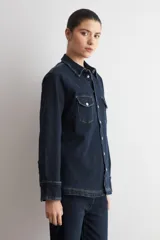 Camisa de jean de corte recto y calce holgado, con cuello clásico, cierre frontal con botones metálicos y dos bolsillos delanteros con solapa y botón.