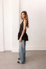 Vestido corto sin mangas de encaje negro, con escote bote y terminación de volados superpuestos.