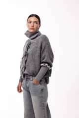 Saco de punto gris con frente abierto, cierre mediante lazos frontales y mangas con puños elásticos. Presenta una textura suave y un diseño de volumen holgado.