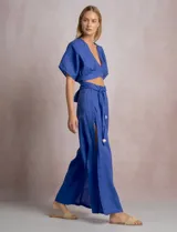 Pantalón palazzo de lino color azul, de tiro alto con cintura elastizada y cinto lazo incorporado con cuentas decorativas en las puntas. Presenta aberturas laterales pronunciadas en las piernas y corte amplio.
