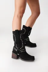 Bota corta de cuero color marrón con efecto gastado, caña media, punta cuadrada y taco bajo. Presenta apliques de tachas plateadas y tiras de cuero con hebillas alrededor del tobillo.