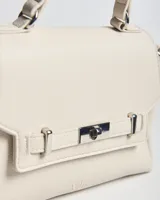 Cartera chica de símil cuero color crudo, con textura granulada, asa superior y correa bandolera regulable y desmontable. Cuenta con solapa frontal con detalle de tira decorativa y cierre giratorio metálico.
